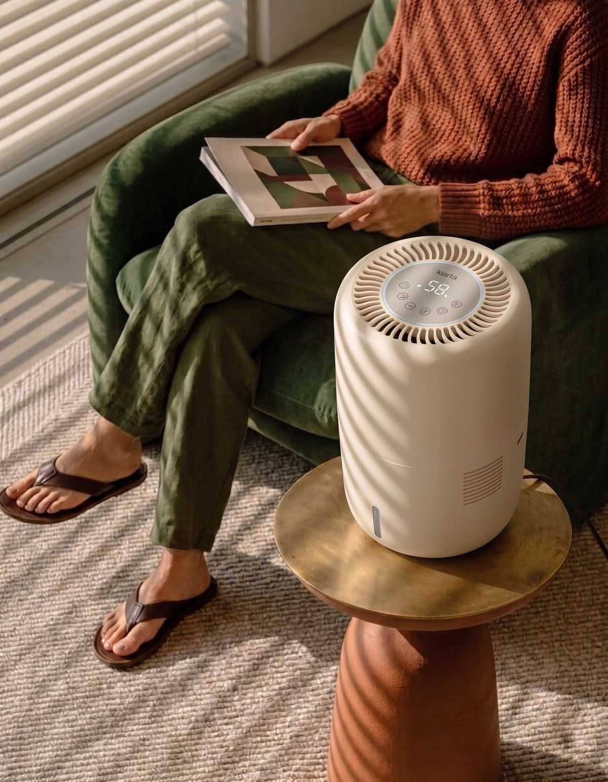 Klarta Humea humidifier in Beige on a side table beside a person reading in an armchair